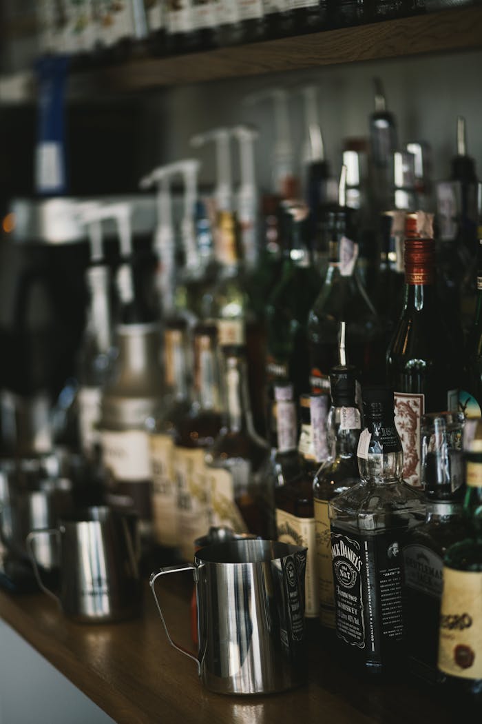 Assorted liquor bottles and glasses in a dimly lit bar setting, showcasing a diverse range of beverages.